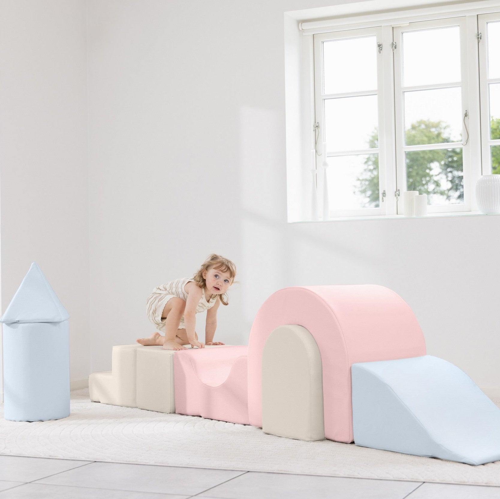 Child playing on a colorful play structure in a bright room with large windows.