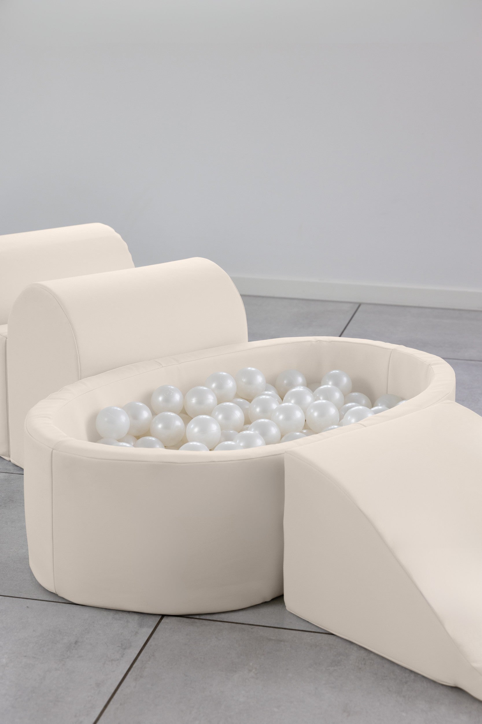Beige ottoman with white pearls on a light gray floor.